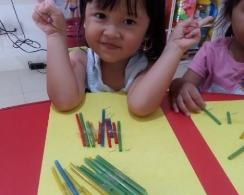 Primary school age child posing for camera while seated at desk in front of crayons and paper
